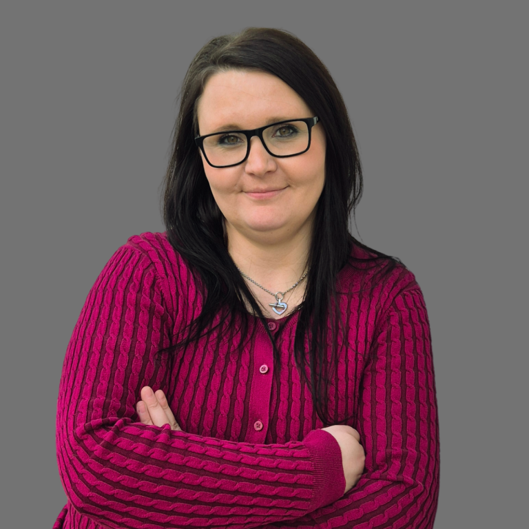 Porträt einer Person mit Brille und langen, dunklen Haaren vor einem grauen Hintergrund.