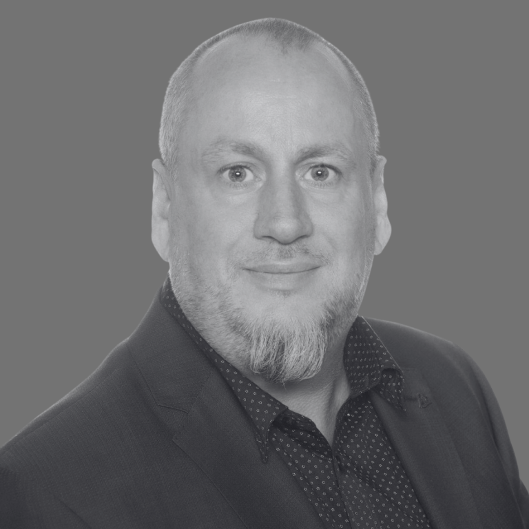 Porträt eines Mannes mit Bart, in einem Anzug und mit neutralem Hintergrund.